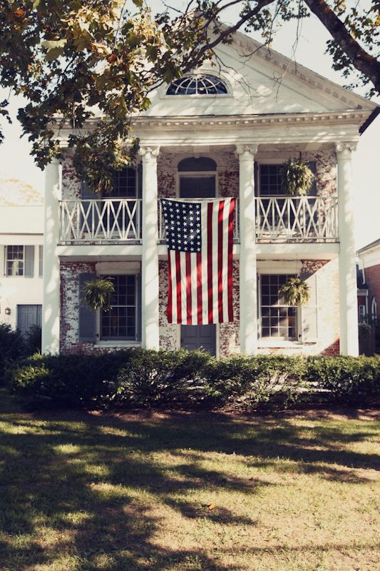 an american flag hanging on the front of a white house with columns and balconies