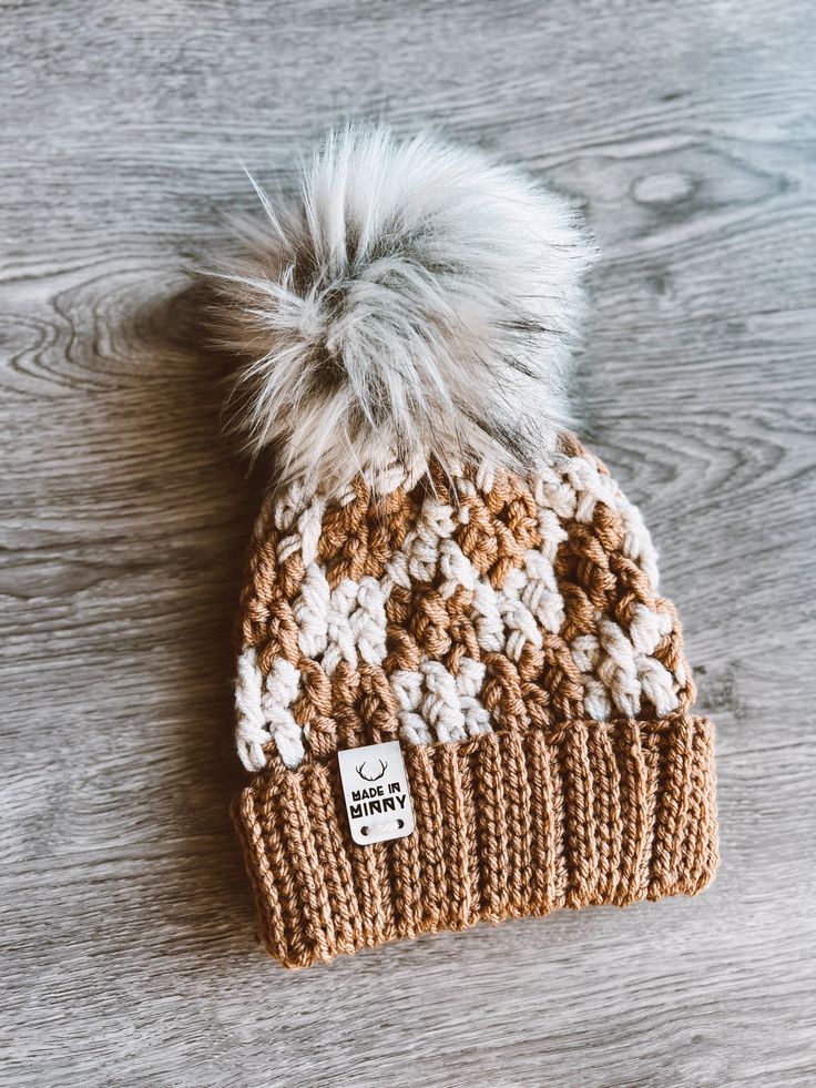 a brown and white knitted hat with a pom - pom on top