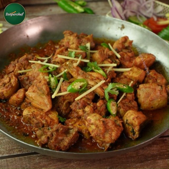 a pan filled with meat and vegetables on top of a wooden table next to green peppers