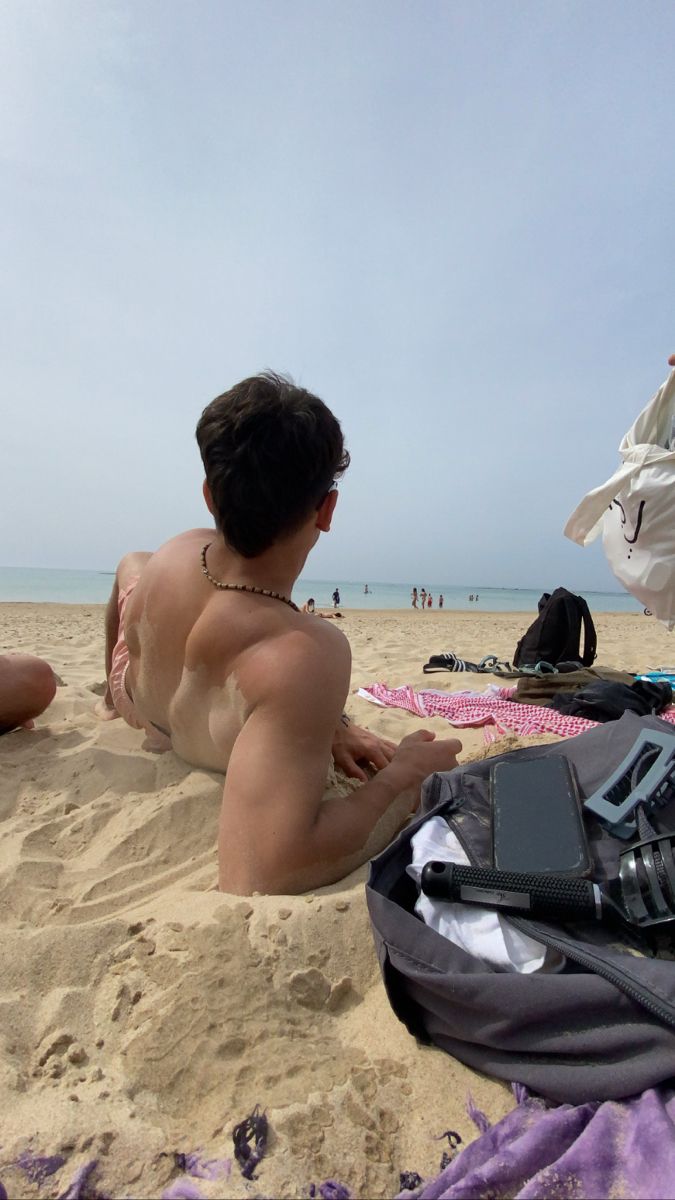 a man sitting on top of a sandy beach next to an open laptop computer bag