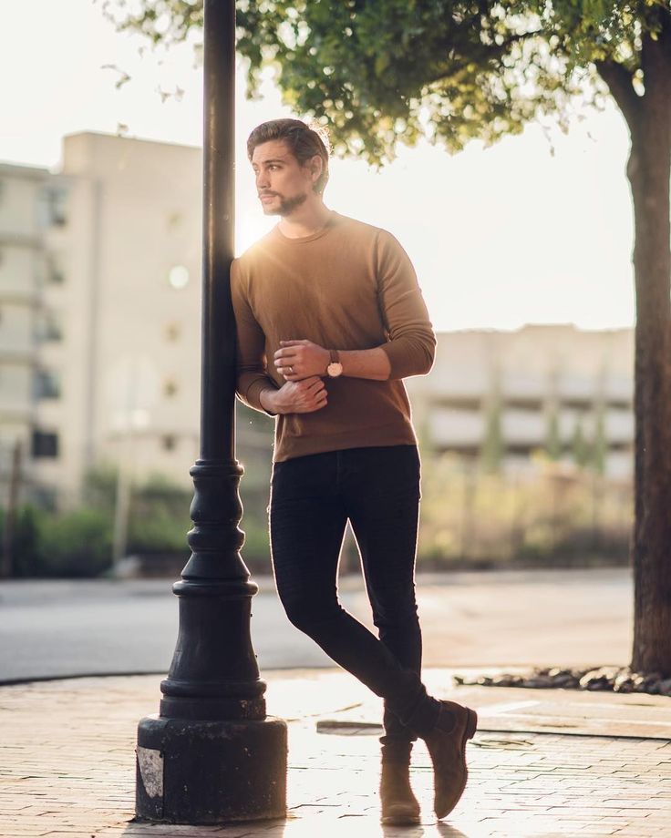 a man standing next to a lamp post on a sidewalk with his hands in his pockets