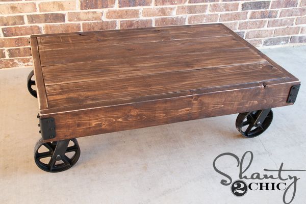 an old wooden cart with wheels is sitting in front of a brick wall and floor