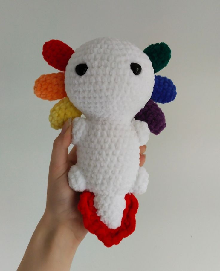 a hand holding a crocheted stuffed animal with multicolored petals on it