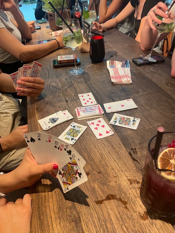 people sitting around a table playing cards with drinks and lemon slices on the table in front of them