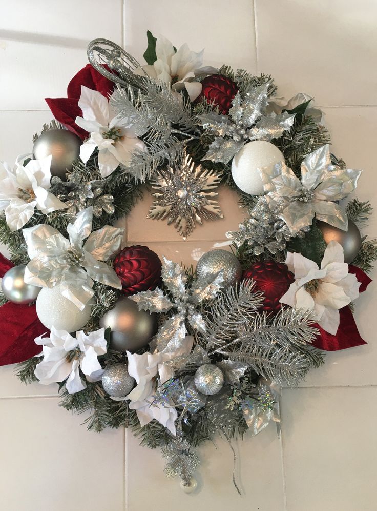 a christmas wreath with silver and red ornaments on the front, hanging from a wall