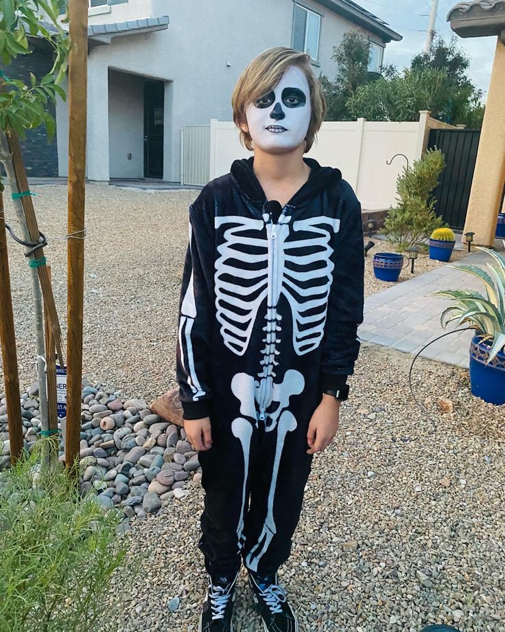 a young boy wearing a skeleton costume in front of a house with his face painted white