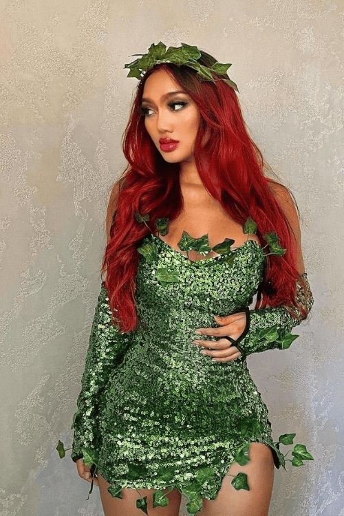 a woman with long red hair and green leaves on her body is posing for the camera