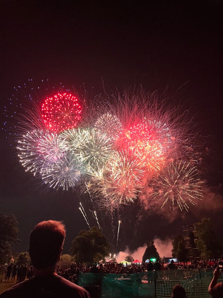 fireworks are lit up in the night sky with people looking at them and watching it