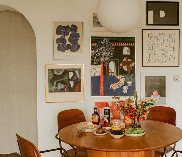 a dining room table with chairs and pictures on the wall above it, along with vases filled with flowers