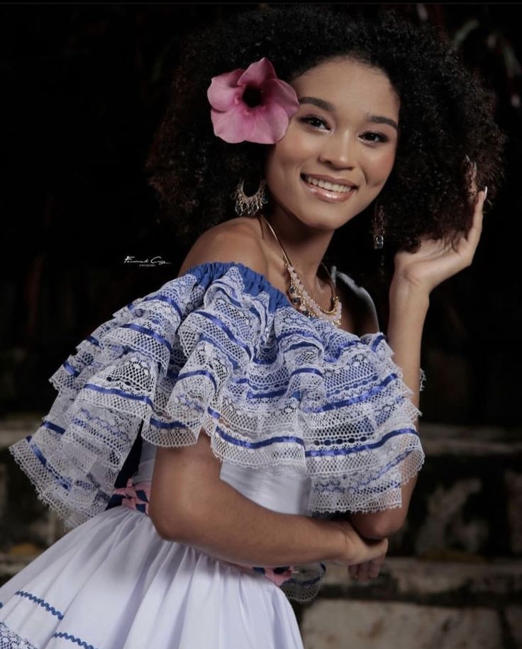 a woman in a white dress with a flower in her hair smiling at the camera