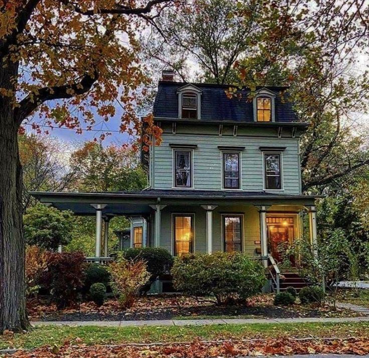 a house with green siding and trees in the front yard, surrounded by leaves on the ground