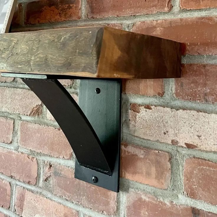 a wooden shelf mounted to the side of a brick wall next to a metal bracket