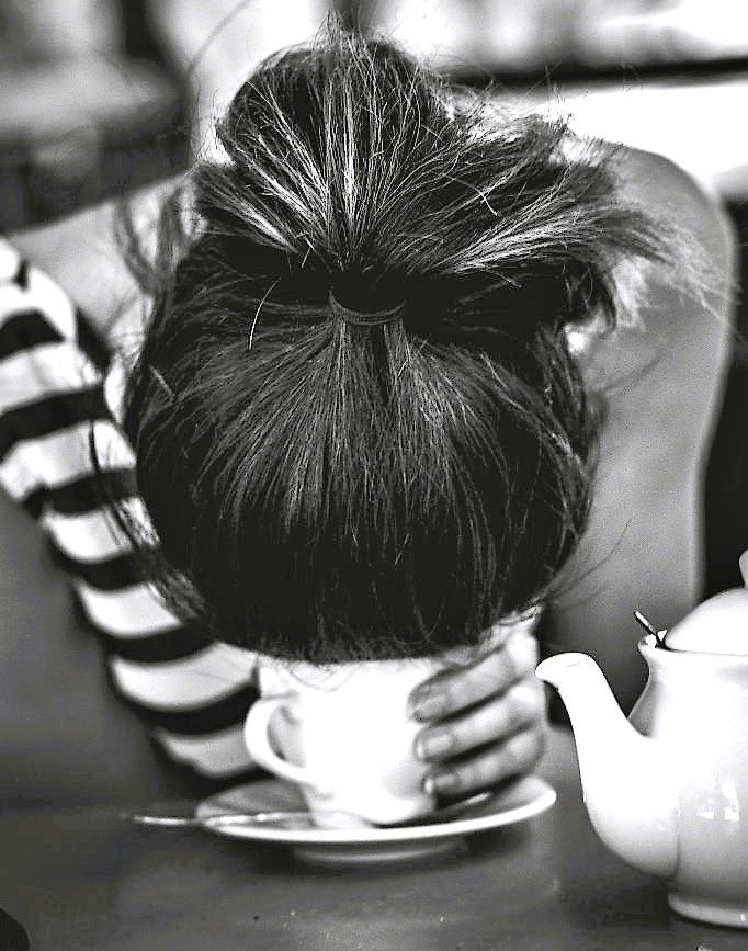 black and white photograph of a woman with her head in a teapot on a table