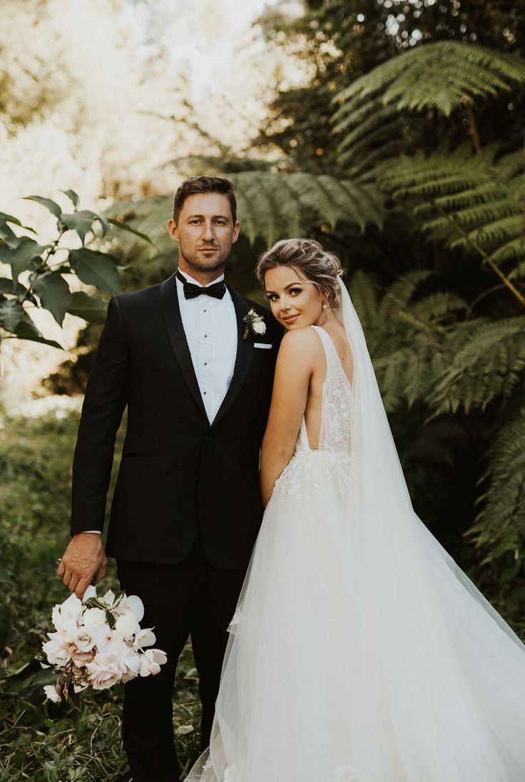 a bride and groom posing for a photo in front of greenery at their wedding