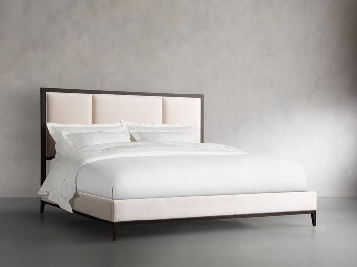 a bed with white sheets and pillows in a room that has concrete walls behind it