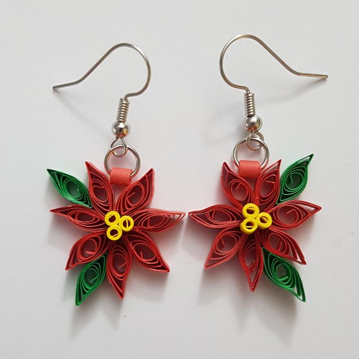 two paper poinsettias with green leaves and yellow centers are hanging from silver earwires