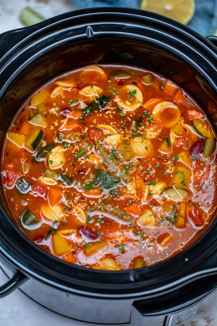 a crock pot filled with vegetable soup and garnished with parsley