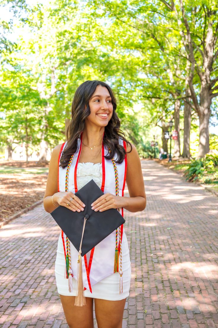 a woman holding a graduation cap and gown in her hands while standing on a brick path