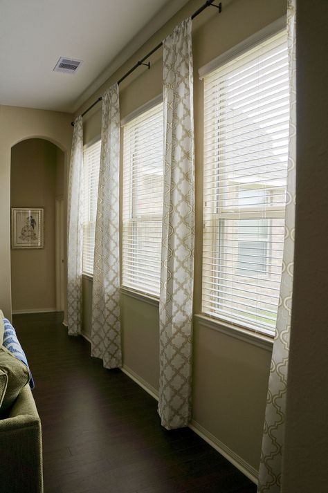 a living room with two couches and three large windows covered in white drapes