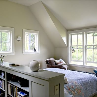 a bed sitting under two windows in a bedroom next to a book shelf filled with books