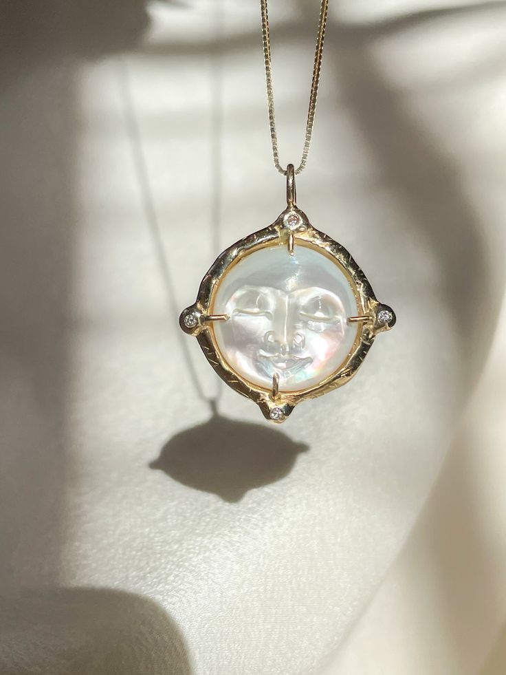 A dreamy 15mm hand-carved Mother of Pearl Moon encircled in gold, set with (4) White Diamonds, set on a solid 14k yellow gold 0.8mm box chain. (Approx. 5.7g.) Inspired in essence by the Impressionist French composer Claude Debussy, Clair de Lune translates to pale blue light or moonlight, and embodies the Divine Feminine energy of the moon, wholly encapsulating the deep sense of serenity found through inner self-awareness, and the strength kept within the gentleness of the heart. Aligns with int Luxury Yellow Gold Sun And Moon Jewelry, Luxury Yellow Gold Jewelry With Sun And Moon Design, Elegant Sun And Moon Medallion Jewelry, Elegant Sun And Moon Design Medallion Jewelry, Elegant Sun And Moon Design Jewelry As Gift, Elegant Sun And Moon Design Jewelry Gift, Elegant Sun And Moon Design Jewelry For Gifts, Celestial Moon Phase White Gold Jewelry, Celestial White Gold Moon Phase Jewelry