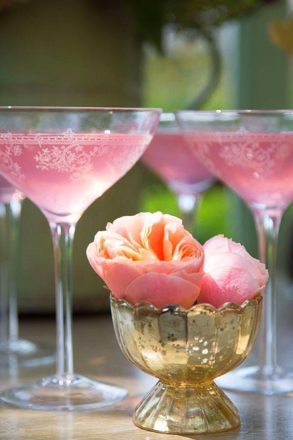 three wine glasses filled with pink liquid and rose petals on the rim, sitting on a table