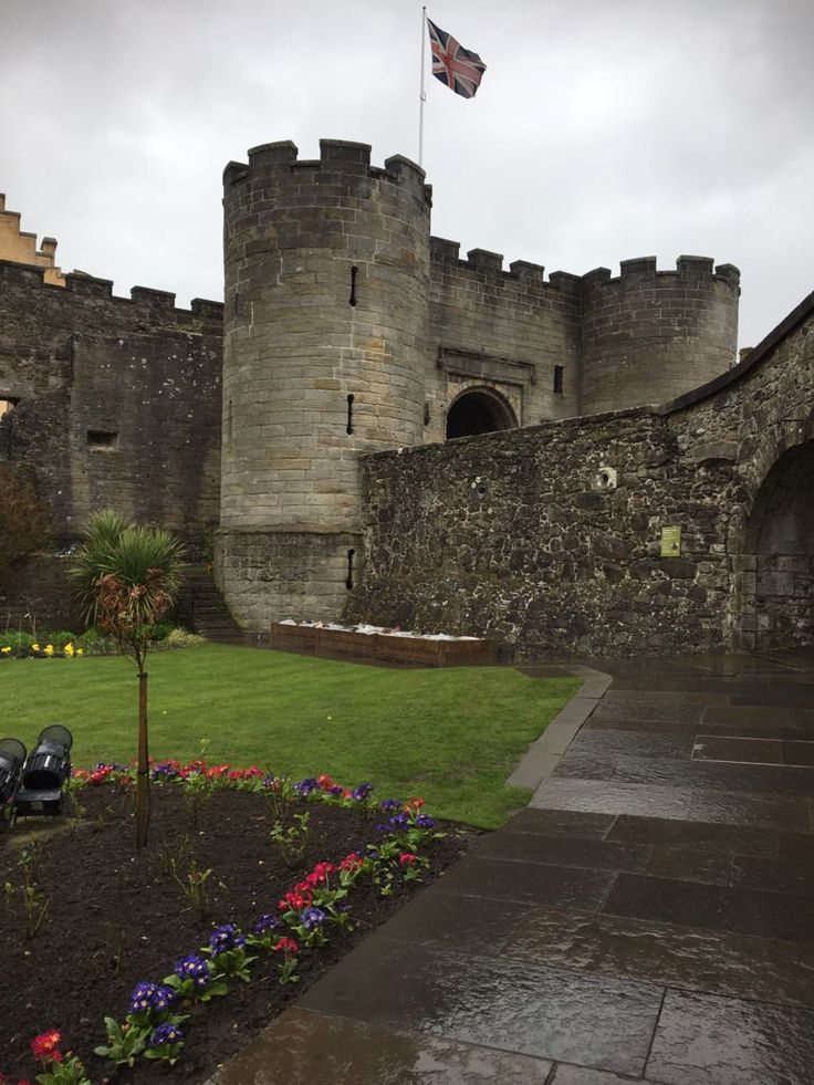 an old castle with flowers in the foreground and a flag flying high above it