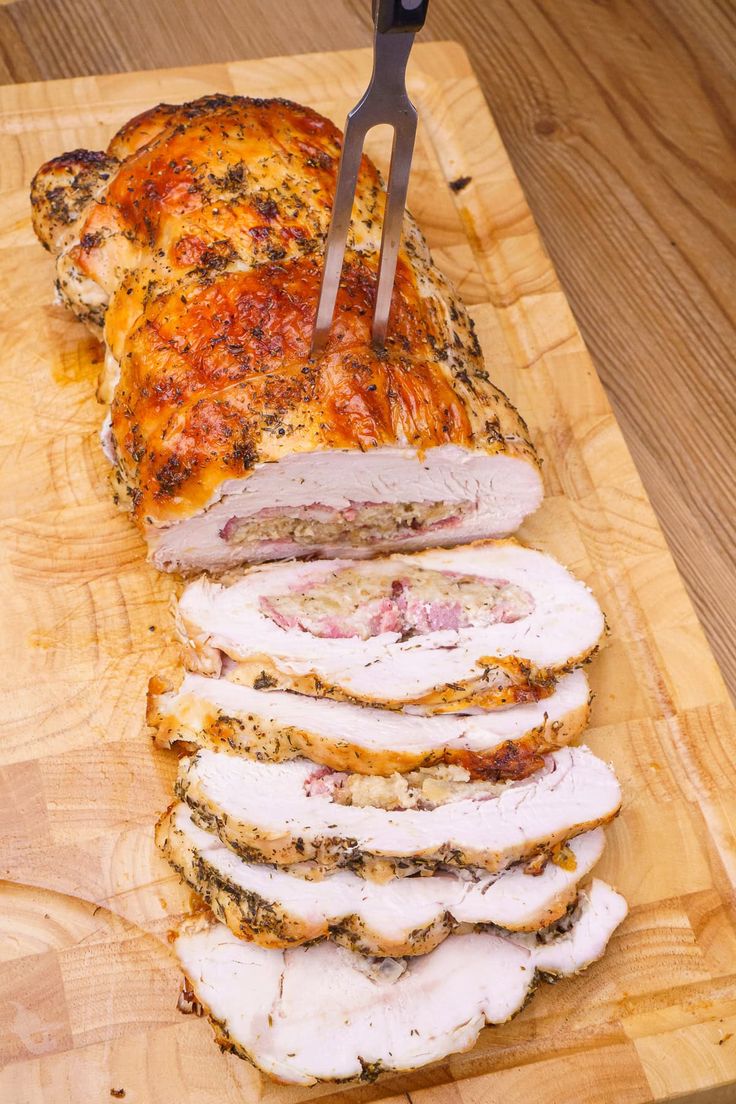 a sliced turkey on a cutting board with a knife stuck in the middle and slices cut out