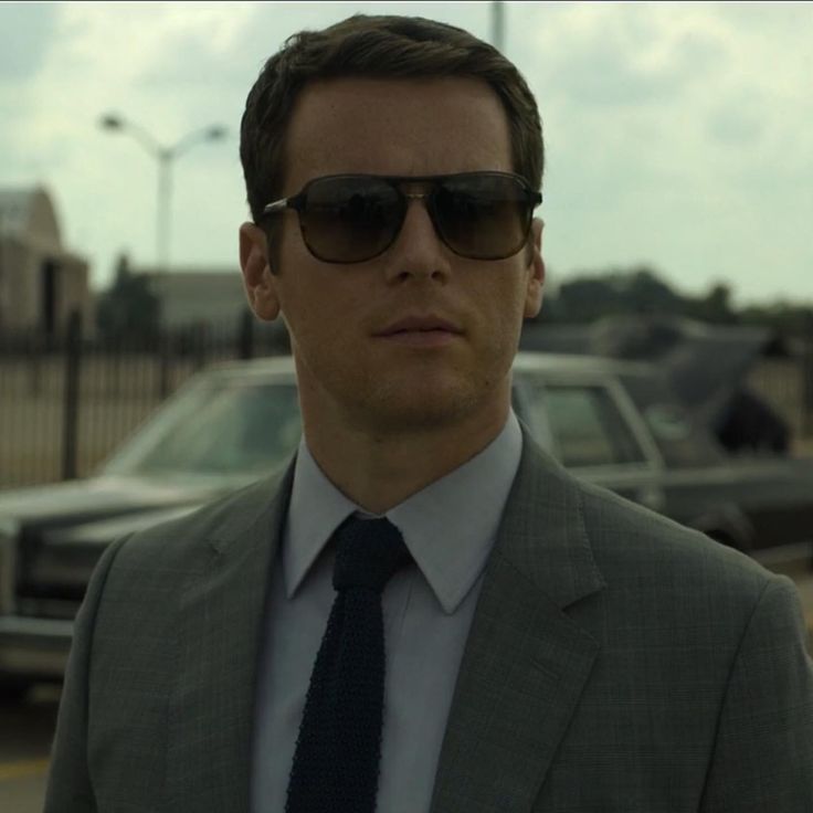 a man in a suit and sunglasses standing next to a car