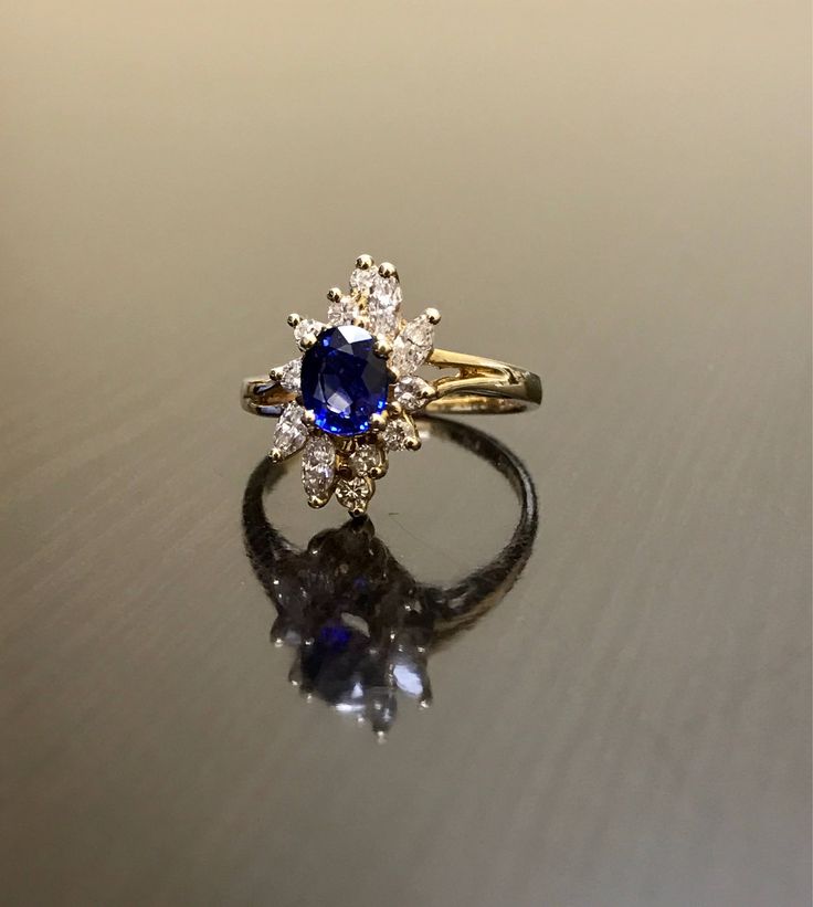 DeKara Designs Clearance Metal- 14K Yellow Gold, .583. Stones- 1 Oval Ceylon Blue Sapphire 0.80 Carats, 4 Marquise Diamonds G Color VS1 Clarity 0.40 Carats, 8 Round Diamonds H Color VS1 Clarity 0.20 Carats. Size- Ring is a 6 3/4, and could be sized up or down at no additional cost! FREE SIZING Handmade 14K Yellow Gold Ceylon Blue Sapphire Halo Diamond Ring. This ring is inspired by the Art Deco era with an enticing fiery oval shaped Ceylon Blue Sapphire. The sapphire is set in between 4 prongs. Blue Diamond Cluster Ring For Formal Occasions, Blue Cluster Ring For Formal Occasions, Formal Blue Diamond Cluster Ring, Formal Blue Cluster Ring, Blue Sapphire Ring Stamped 14k, Blue Diamond Jewelry Stamped 14k, Blue 14k Gold Ring Stamped 14k, Blue 14k Gold Rings For Anniversary, Blue 14k Stamped Promise Ring