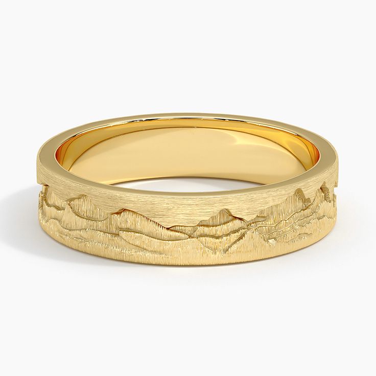 a yellow gold wedding band with mountains in the background and waves on it's surface