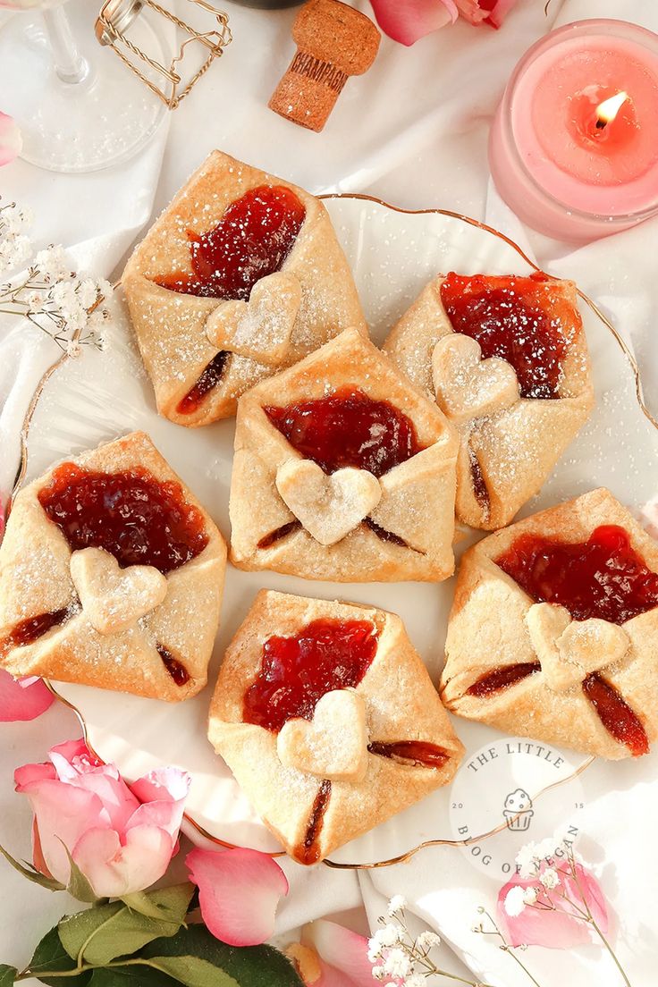 small pastries on a plate with strawberry jam in the middle and pink flowers around them