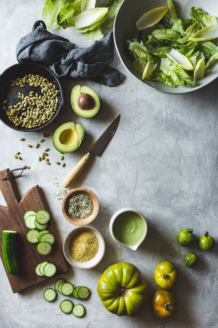 an assortment of fresh vegetables are laid out on a table with knifes and bowls