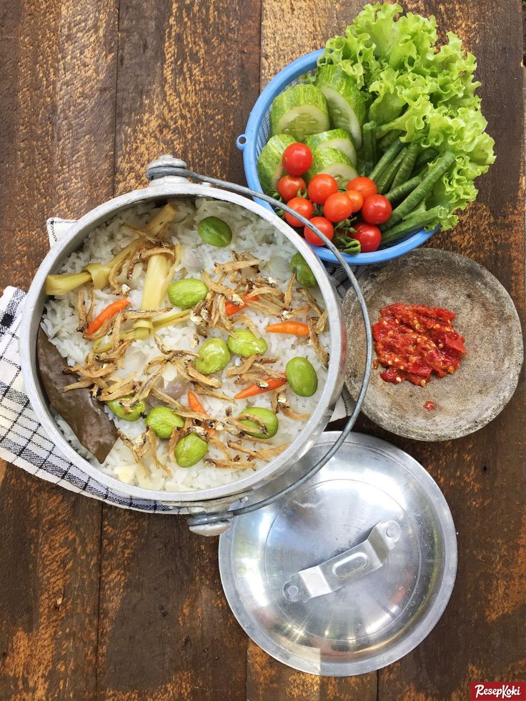 two bowls filled with rice, vegetables and sauce on top of a wooden table next to a bowl of lettuce