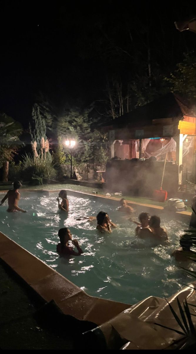 people are in the pool at night with steam coming from the water and lights on