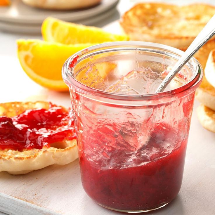 a glass jar filled with jam next to lemon slices and bread on a cutting board