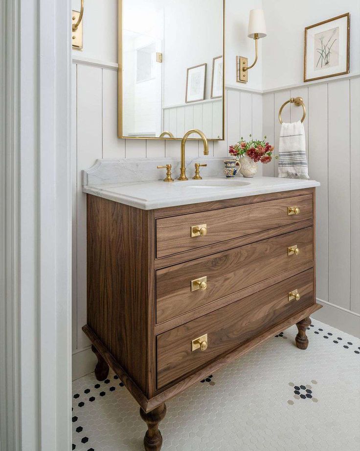 a bathroom vanity with marble counter top and gold handles, along with framed pictures on the wall