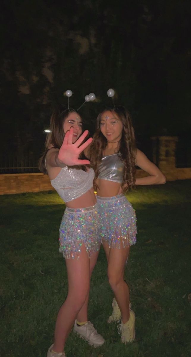 two young women in sequin skirts posing for the camera at night with their hands up