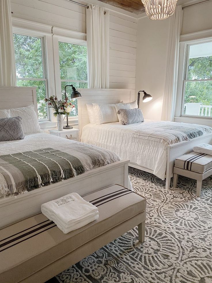 two beds in a bedroom with white walls and flooring next to each other on either side of the windows