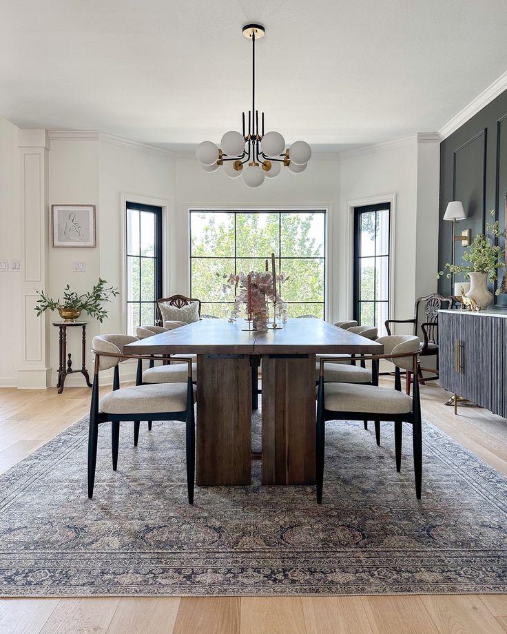 a large dining room table with chairs and a rug in front of the table is surrounded by windows