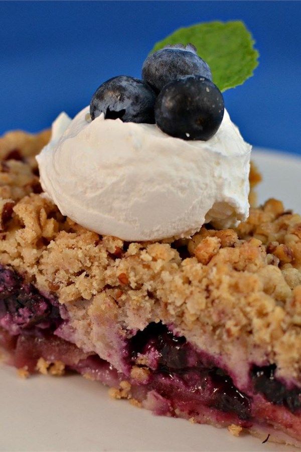 a slice of blueberry crumb pie on a plate with whipped cream and mint leaves