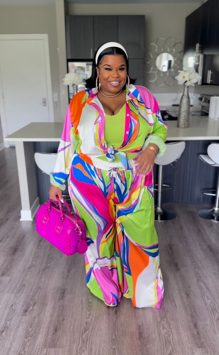 a woman standing in front of a kitchen counter wearing a colorful dress and carrying a pink purse