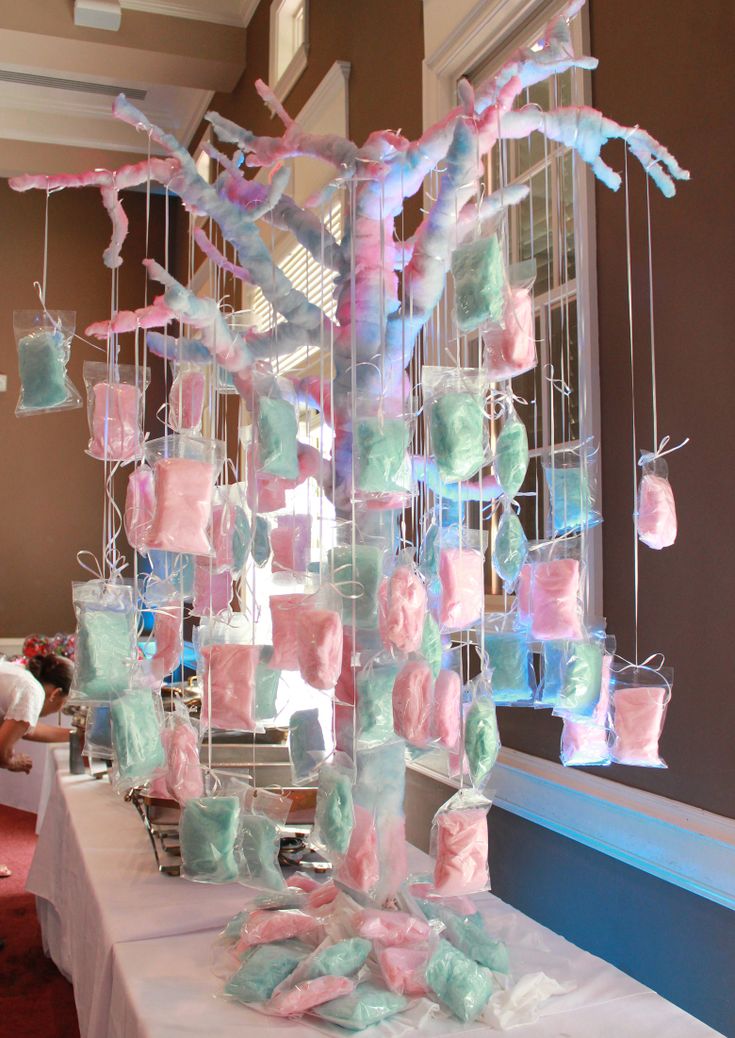 a white table topped with lots of pink and blue items next to a tree filled with baby's breath