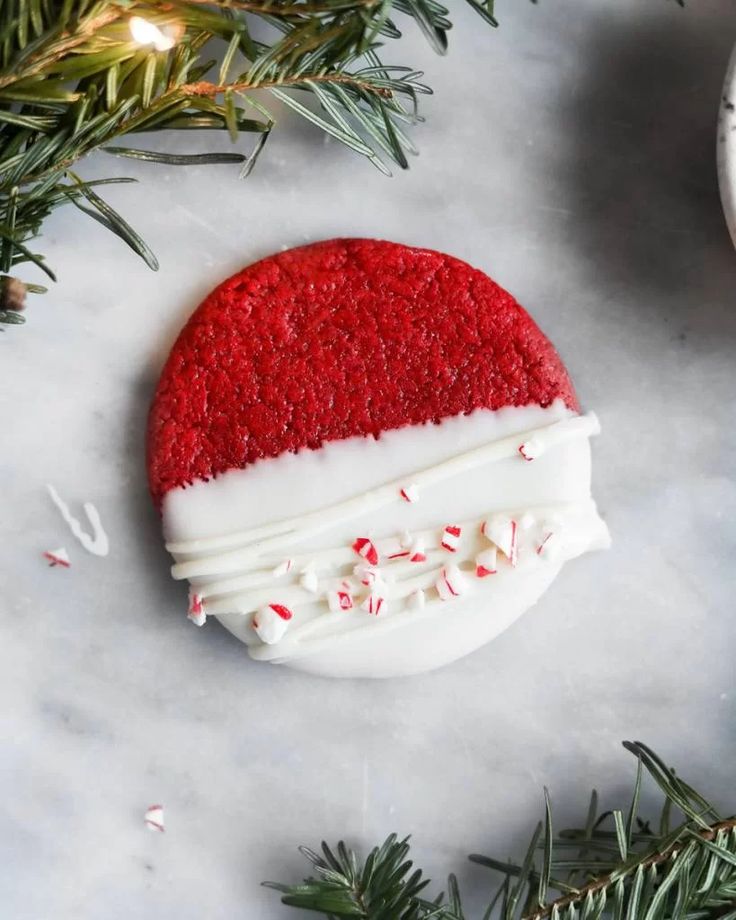 a red and white christmas cookie with sprinkles on it next to evergreen branches