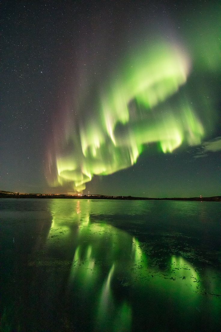 an image of the aurora bore in the sky above water with reflections on the surface