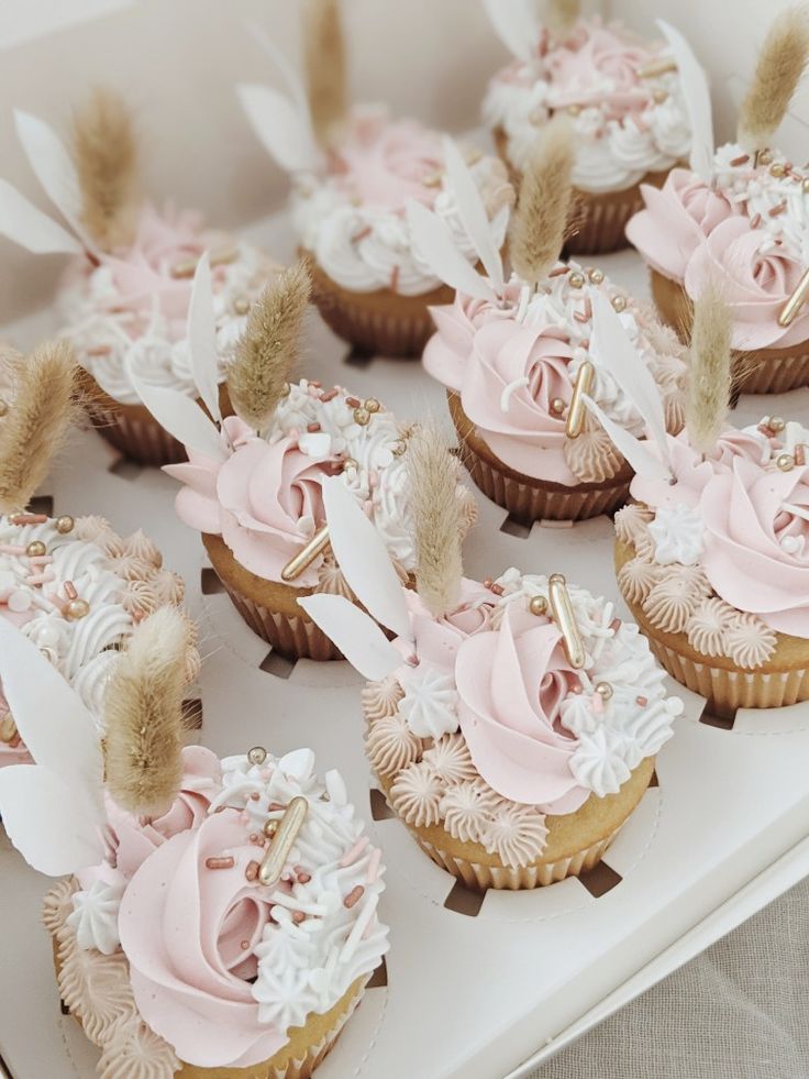 cupcakes decorated with pink frosting and feathers on a white tablecloth covered tray