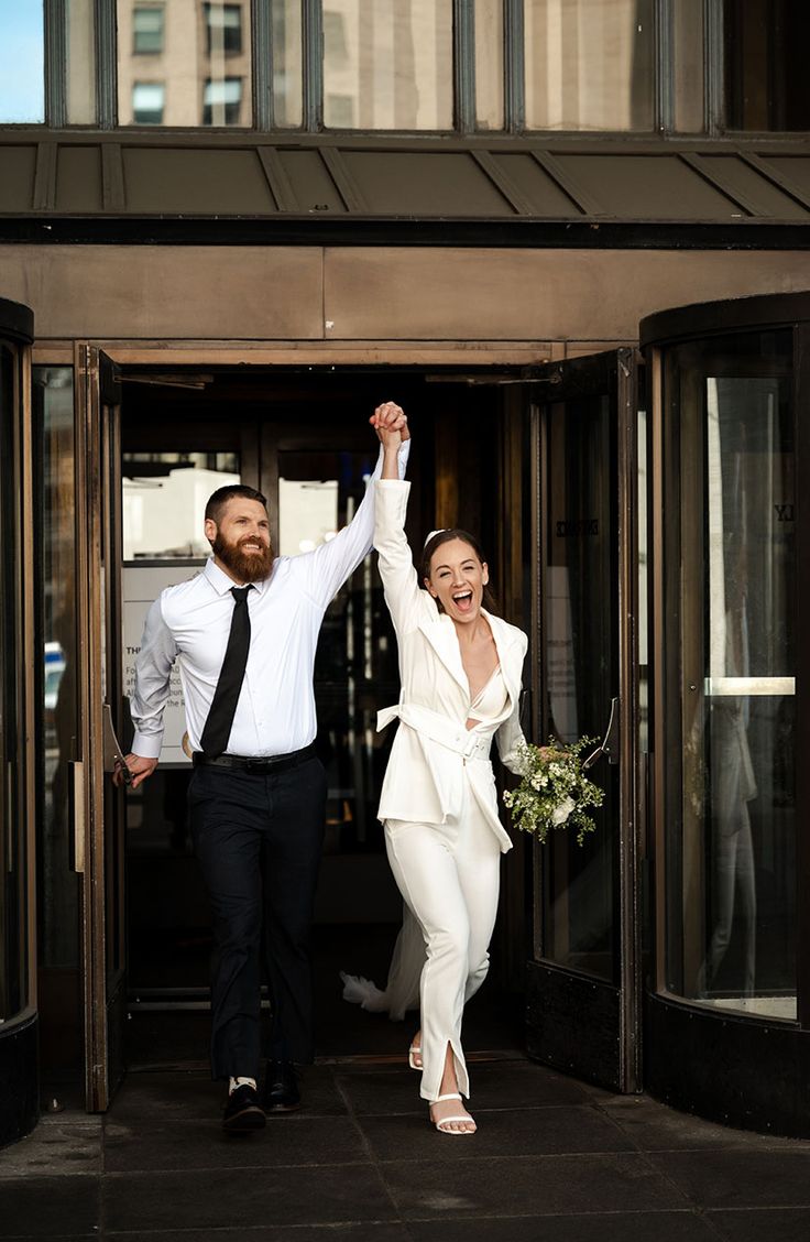 a man and woman are walking out of a building with their hands in the air