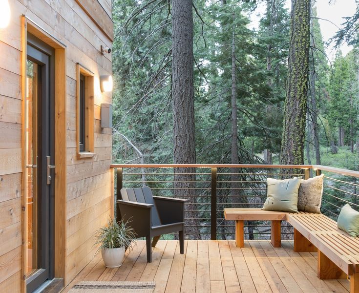 a wooden deck with two benches on it and trees in the backgrouds