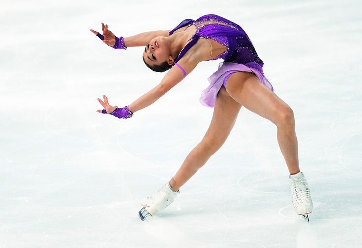 a female figure skating on the ice in a purple dress and white boots with her arms outstretched