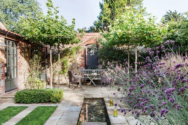 an outdoor garden with purple flowers and greenery in the back yard, surrounded by brick buildings